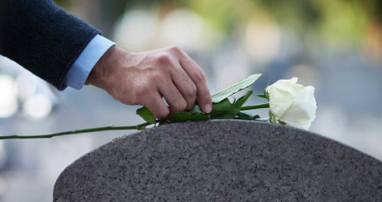 Eine Hand legt eine weiße Rose auf einen Grabstein