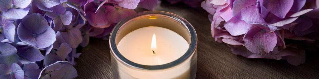 Brennende Kerze in einem Glas zwischen Hortensienblüten
