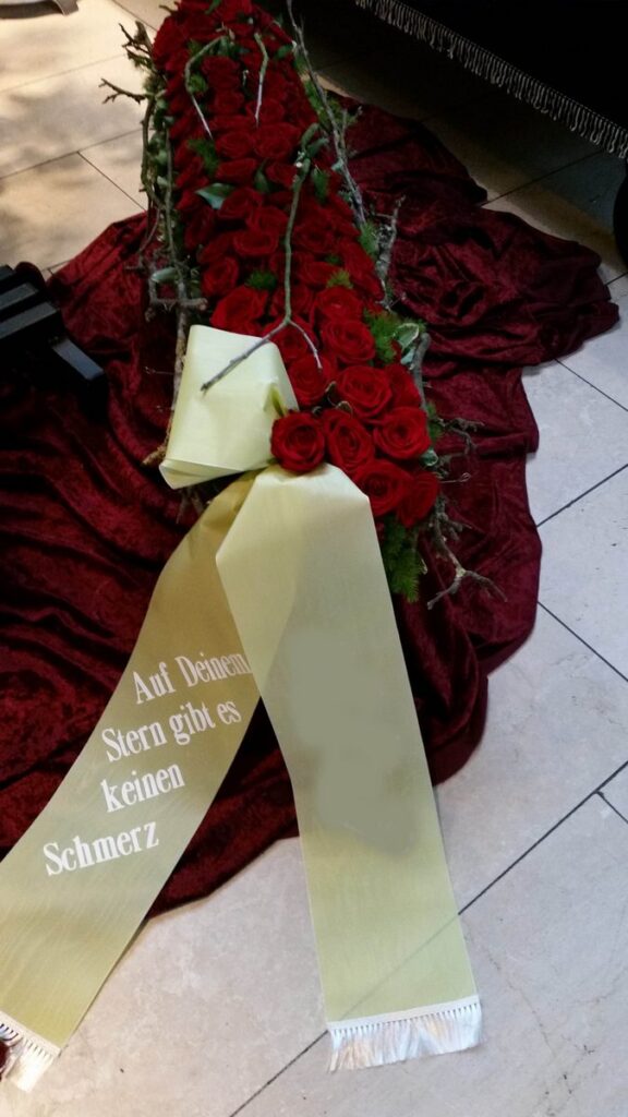 Gesteck aus roten Rosen mit beschrifteter Trauerschleife