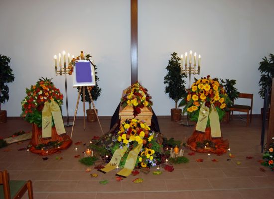 Trauerhalle mit Sarg und Blumenschmuck in Herbstfarben, Kränze auf Ständern