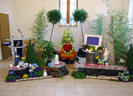 Trauerhalle mit Sarg und einer Dekoration aus Pflanzen, Steinen und Blumen