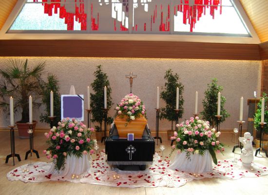 Trauerhalle mit Sarg und Blumenschmuck in Rosa, Kerzen auf beiden Seiten