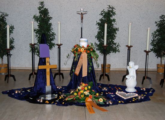 Urne auf blauem Tuch mit Blumenschmuck und Kerzen in der Trauerhalle