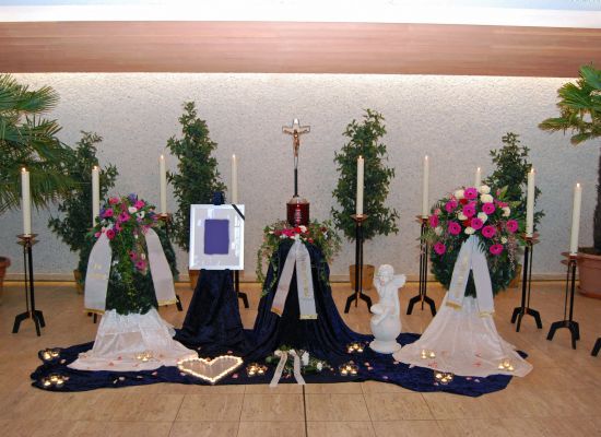 Urne auf dunkelblauem Tuch mit Blumenschmuck und kleinen Lichtern