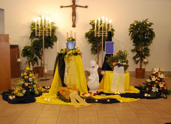 Urne mit gelbem Blumenschmuck und gelben Tüchern in der Trauerhalle