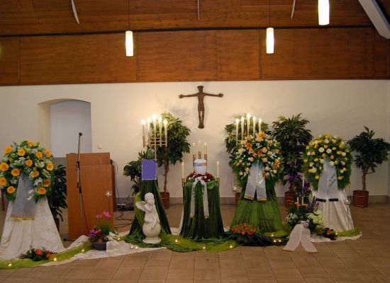 Urne mit Blumenschmuck in Orange und Grün, daneben Kerzen und eine Figur