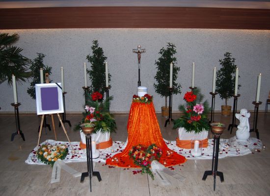 Urne auf orangefarbenem Tuch mit rotem Blumenschmuck