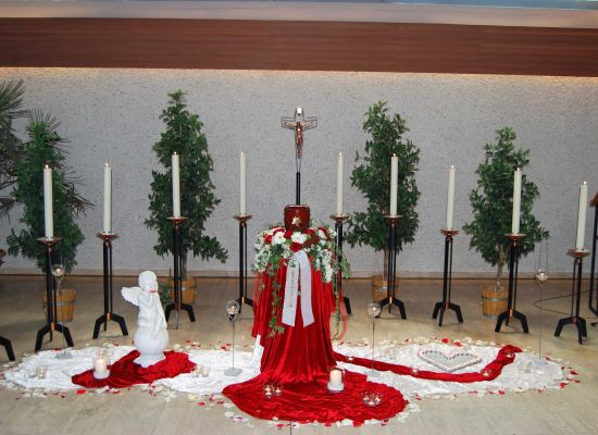 Urne auf rotem Tuch mit weißen Rosen und Kerzen